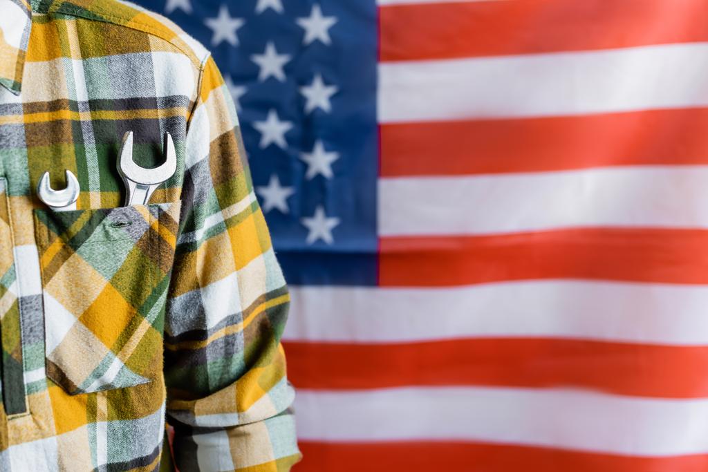 частичный вид бригадира с ключами в кармане клетчатой рубашки рядом с размытым флагом США, концепция Дня труда - Фото, изображение