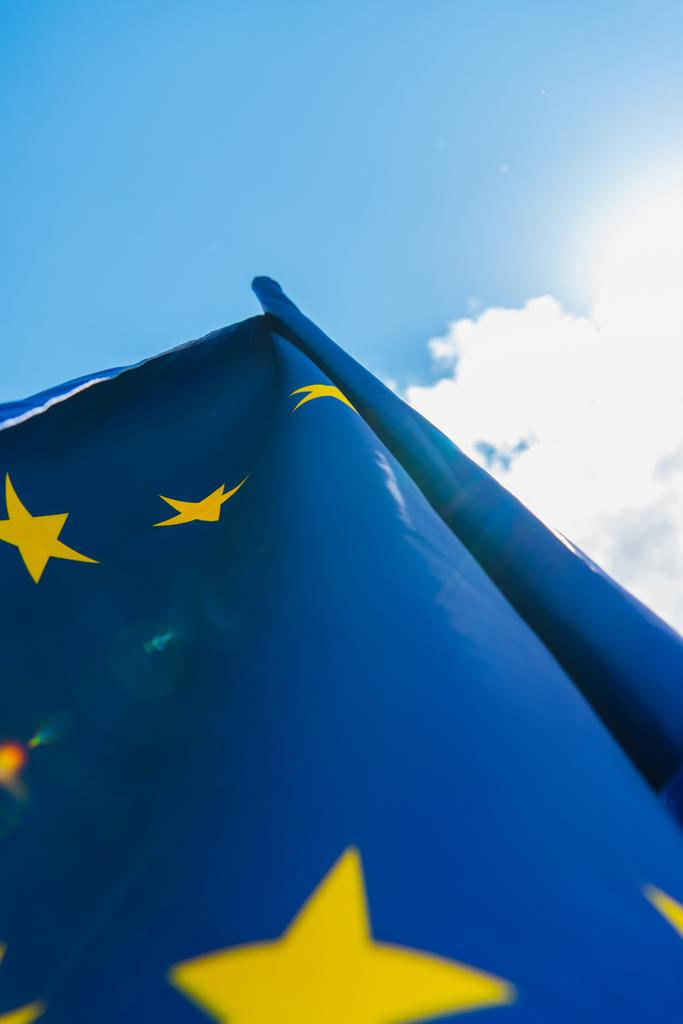 vista inferior de la bandera azul de la unión europea contra el cielo con nubes - Foto, Imagen