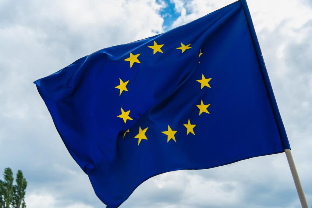 низький кут зору європейського прапора Союзу з жовтими зірками на небі
  - Фото, зображення