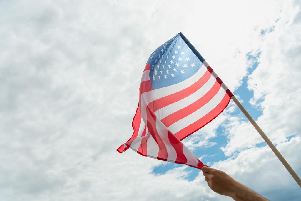 vista recortada del hombre sosteniendo bandera americana con estrellas y rayas contra el cielo nublado  - Foto, Imagen
