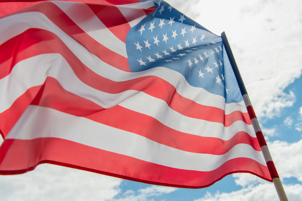 vista de ángulo bajo de la bandera americana con estrellas y rayas contra el cielo nublado  - Foto, Imagen