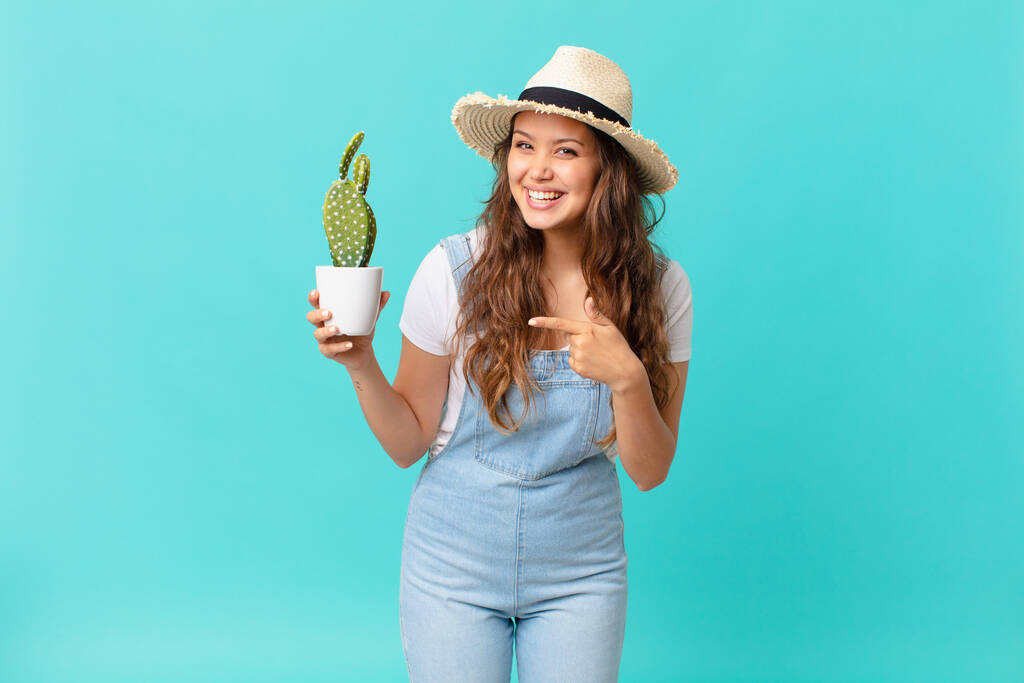 young pretty woman looking excited and surprised pointing to the side and holding a cactus - Photo, Image
