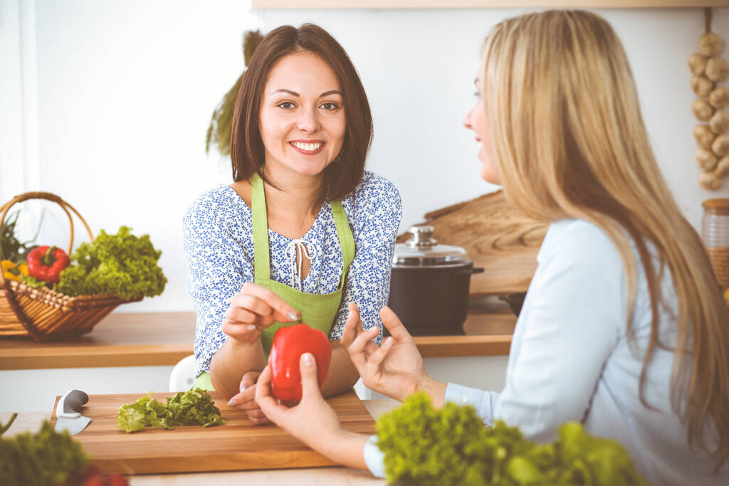Дві жінки вибирають рецепт і інгредієнти для смачної їжі, сидячи за кухонним столом. Вегетаріанська концепція. - Фото, зображення
