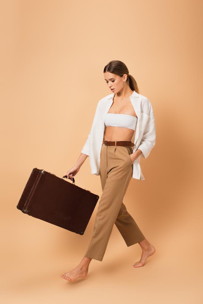 パンツの若い女性とボタンなしのシャツ歩く裸足でヴィンテージスーツケースとともにベージュの背景 - 写真・画像