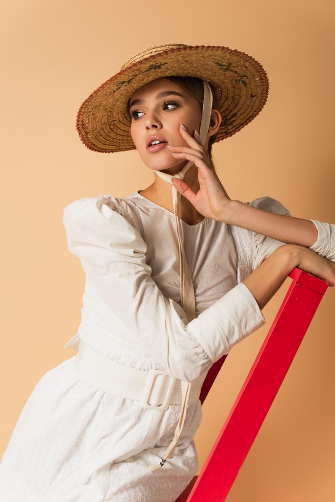 Kırmızı merdivende bej rengi elbisesi ve hasır şapkası olan genç kadın. - Fotoğraf, Görsel