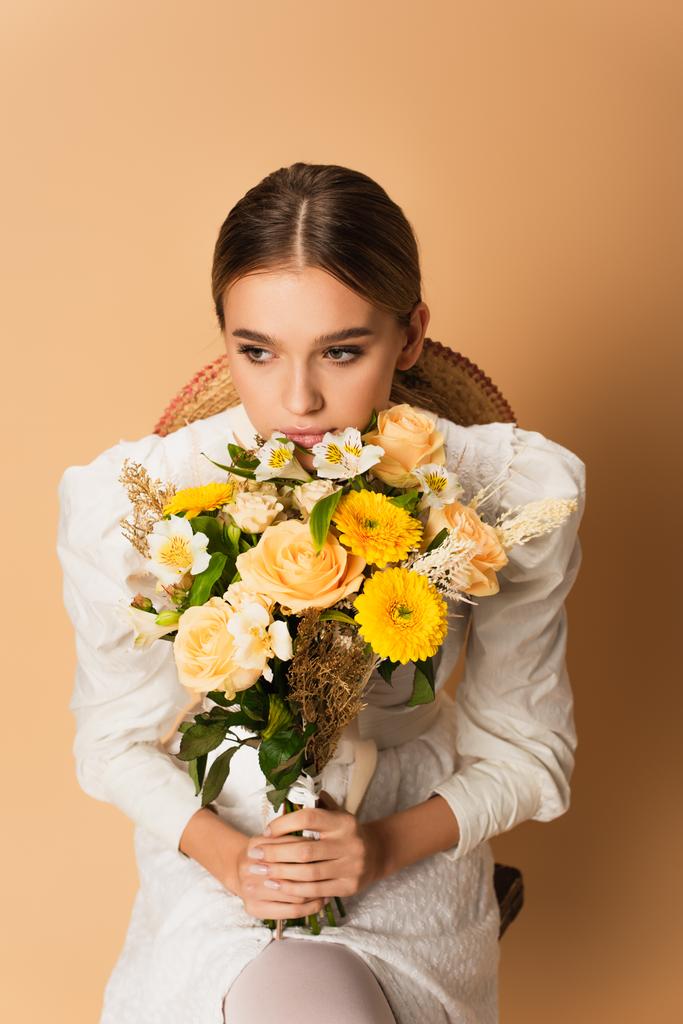 giovane donna in abito bianco che tiene bouquet con fiori diversi sul beige - Foto, immagini