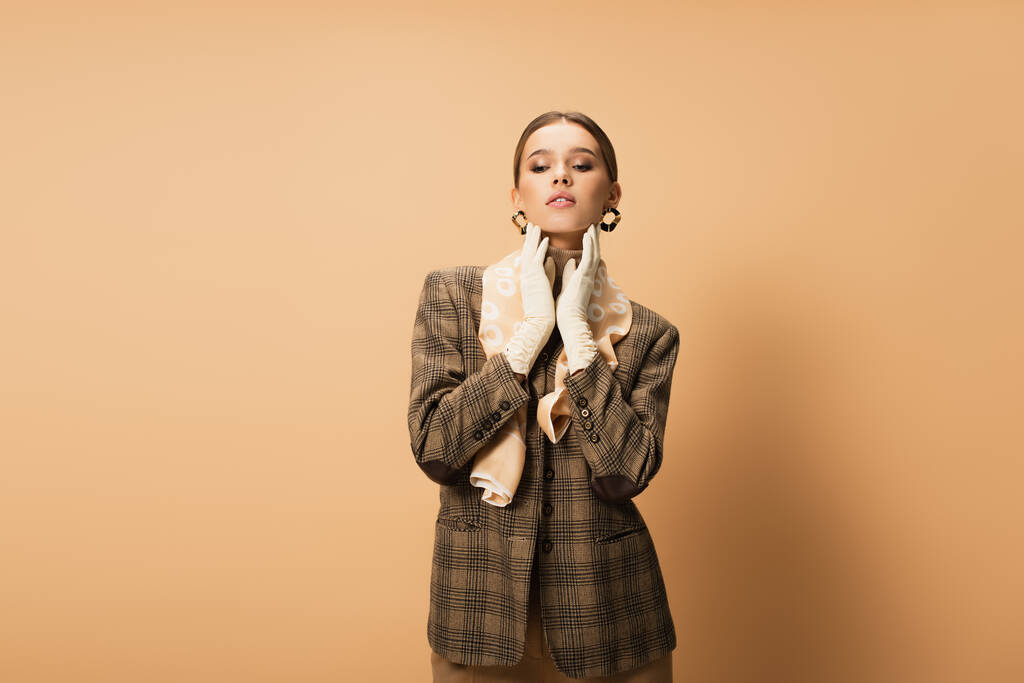 stylish woman in checkered blazer and white gloves posing on beige - Photo, Image