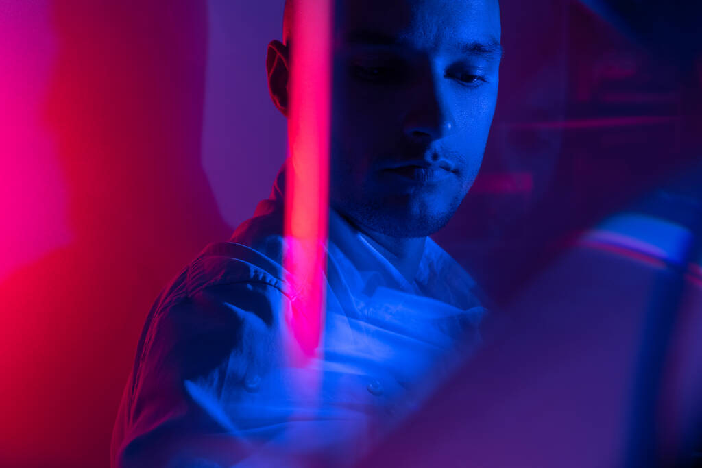 Close-up cinematic portrait of handsome young man in neon blue pink lighted room, stylish male model indoors. Reflection effect - Photo, Image
