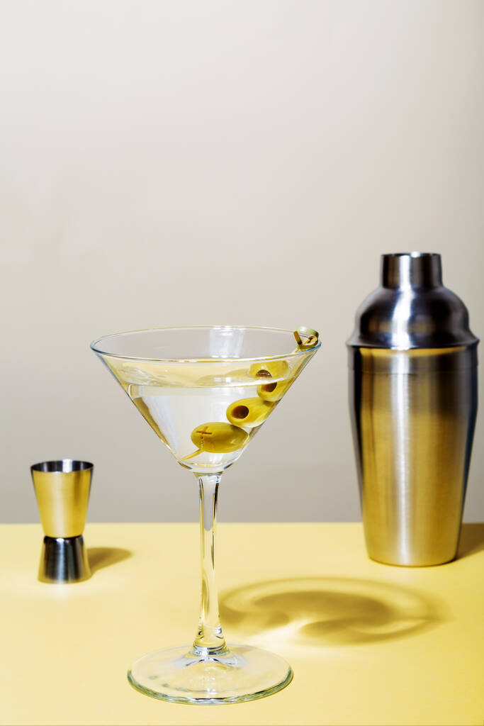Glas martini cocktail met groene olijven. Vlakbij jigger en shaker. Focus op schaduwen - Foto, afbeelding