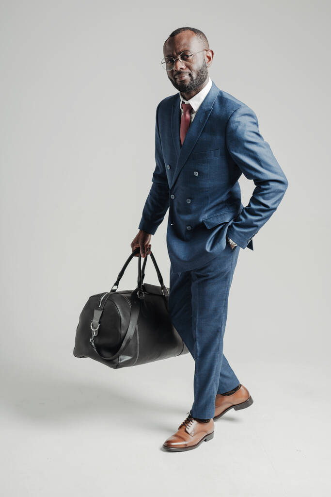 Афроамериканский бизнесмен в костюме держит сумку с вещами в руках и отправляется в деловую поездку. - Фото, изображение