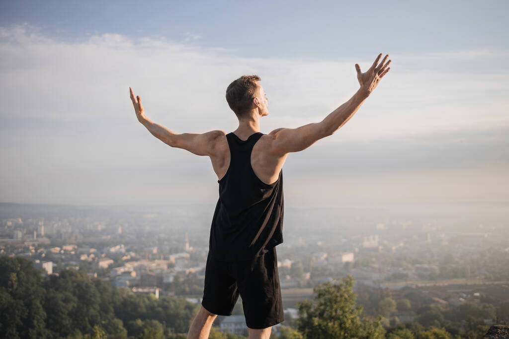 Takaisin näkymä komea lihaksikas mies rentouttava korkealla kukkulalla, seisoo kädet ojennettuina - Valokuva, kuva