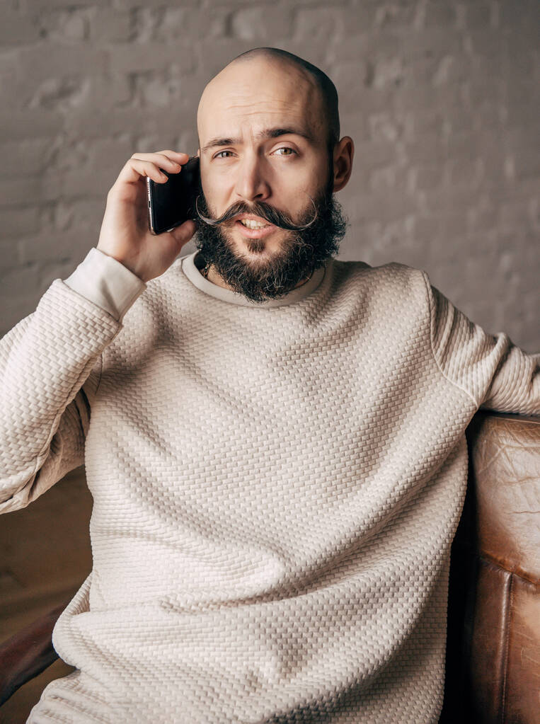 un joven calvo blanco con barba está hablando por teléfono en la habitación - Foto, imagen