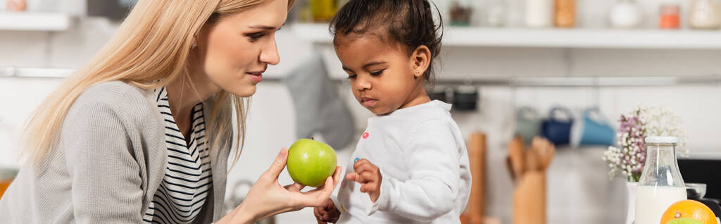mother giving apple to adopted african american kid in kitchen, banner - Photo, Image