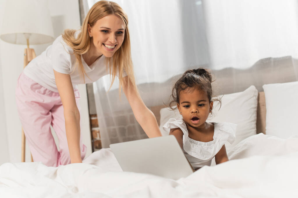 щаслива мати і прийнята афроамериканська дівчина дивиться фільм на ноутбук у спальні
  - Фото, зображення