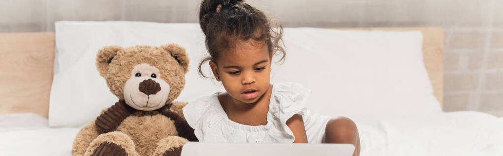 Afro-Amerikalı çocuk dizüstü bilgisayarında yumuşak oyuncağın yanında film izliyor. - Fotoğraf, Görsel