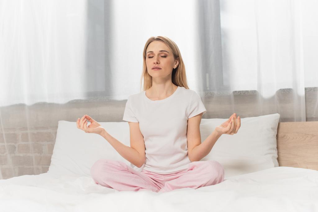 szőke nő pizsamában meditál az ágyban - Fotó, kép