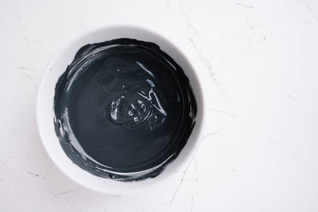Black clay texture. Mud mask for face and body in a bowl. Natural spa treatment. Black and white stylish background. Cosmetology skin treatment - Photo, Image