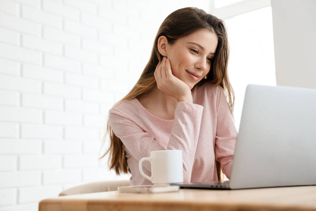 Boldog fiatal fehér nő visel lounge ruhák ül az asztalnál laptoppal, tanulás, videohívás - Fotó, kép