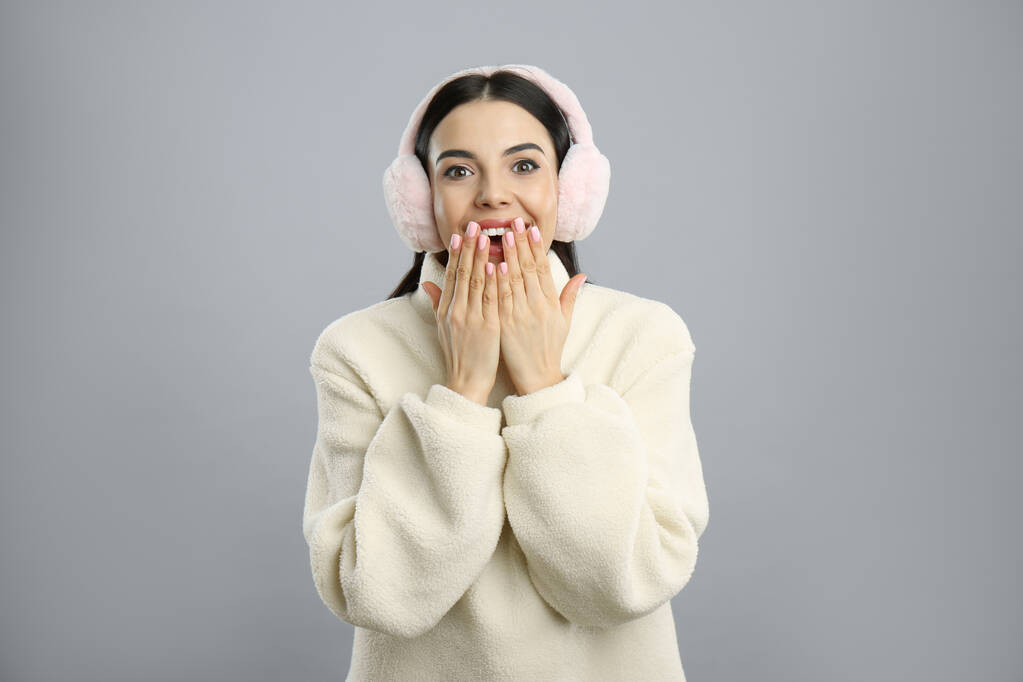 mooie jonge vrouw dragen oorkappen op licht grijze achtergrond - Foto, afbeelding