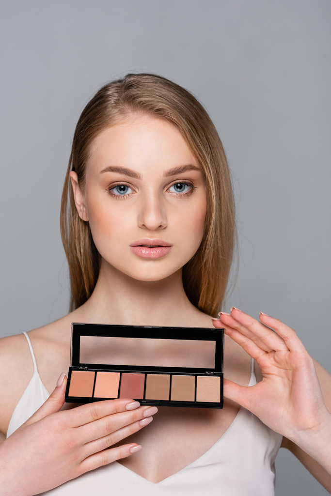 hübsche Frau hält kosmetische Rouge-Palette isoliert auf grau - Foto, Bild