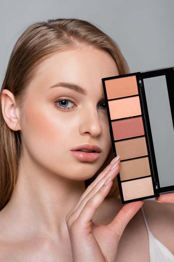 junge hübsche Frau hält Kosmetikpalette isoliert auf grau - Foto, Bild