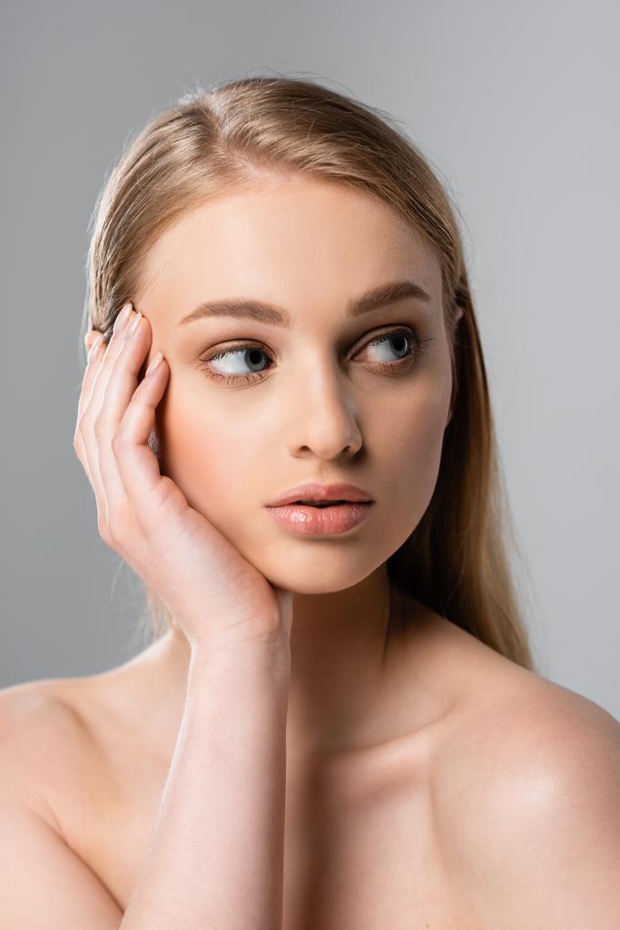 young woman touching face and looking away isolated on grey - Photo, Image