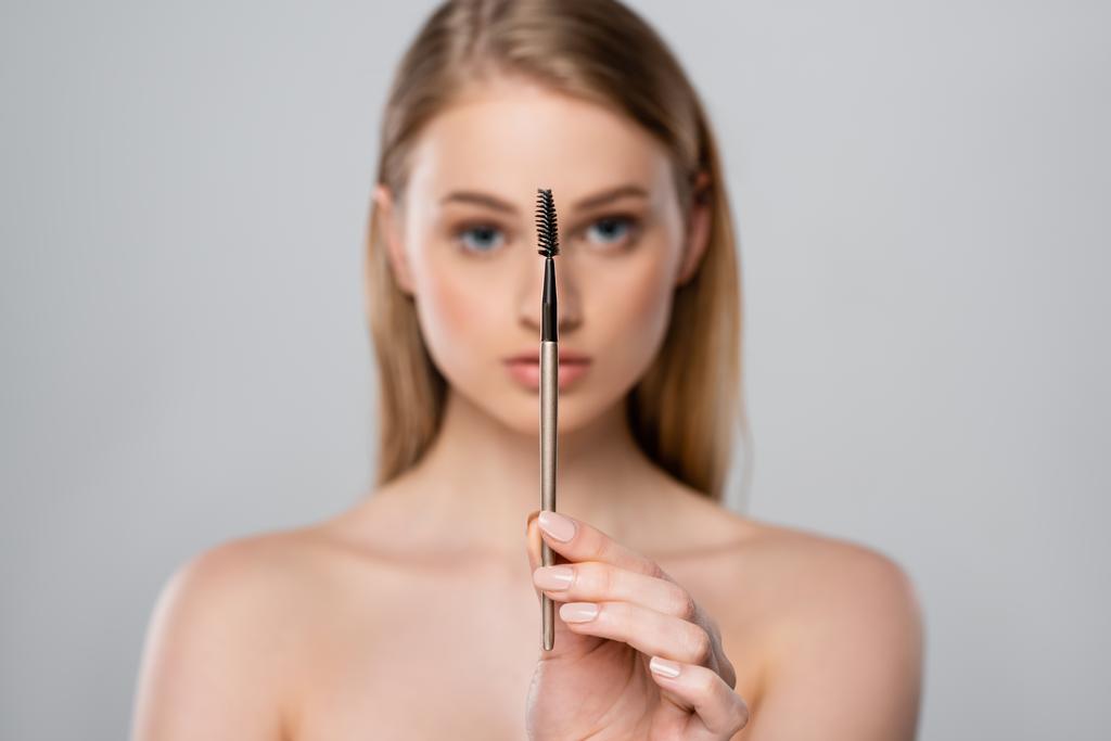 verschwommen junge Frau mit nackten Schultern hält Augenbrauenbürste isoliert auf grau - Foto, Bild