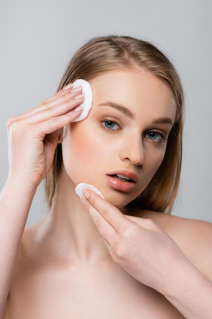 young woman with bare shoulders removing makeup with cotton pads isolated on gray - Photo, Image