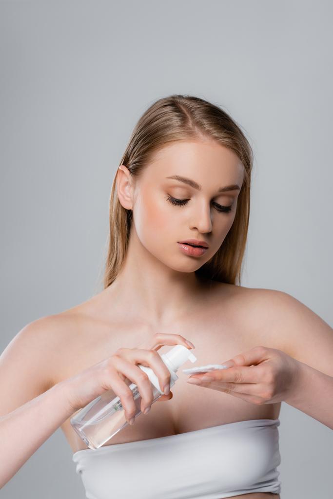 young woman with bare shoulders applying micellar water on cotton pad isolated on grey - Photo, Image