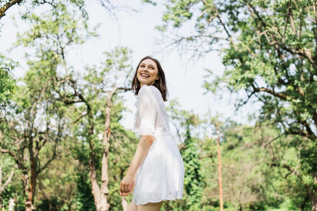 Szczęśliwa kobieta w białej sukience stojąca w letnim parku  - Zdjęcie, obraz