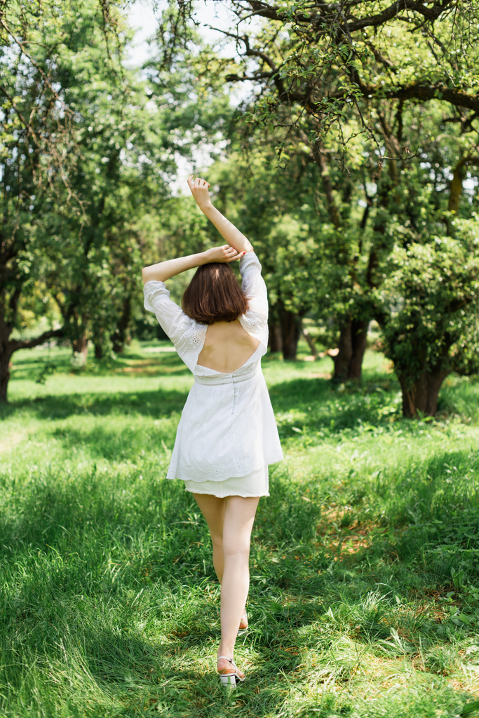 Πίσω όψη της μελαχρινής γυναίκας σε λευκό φόρεμα περπάτημα στο πάρκο  - Φωτογραφία, εικόνα