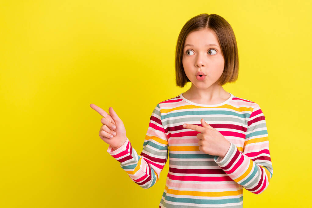 Foto van geschokt verbaasd klein meisje wijzen vinger lege ruimte look nieuws verkoop geïsoleerd op gele kleur achtergrond - Foto, afbeelding