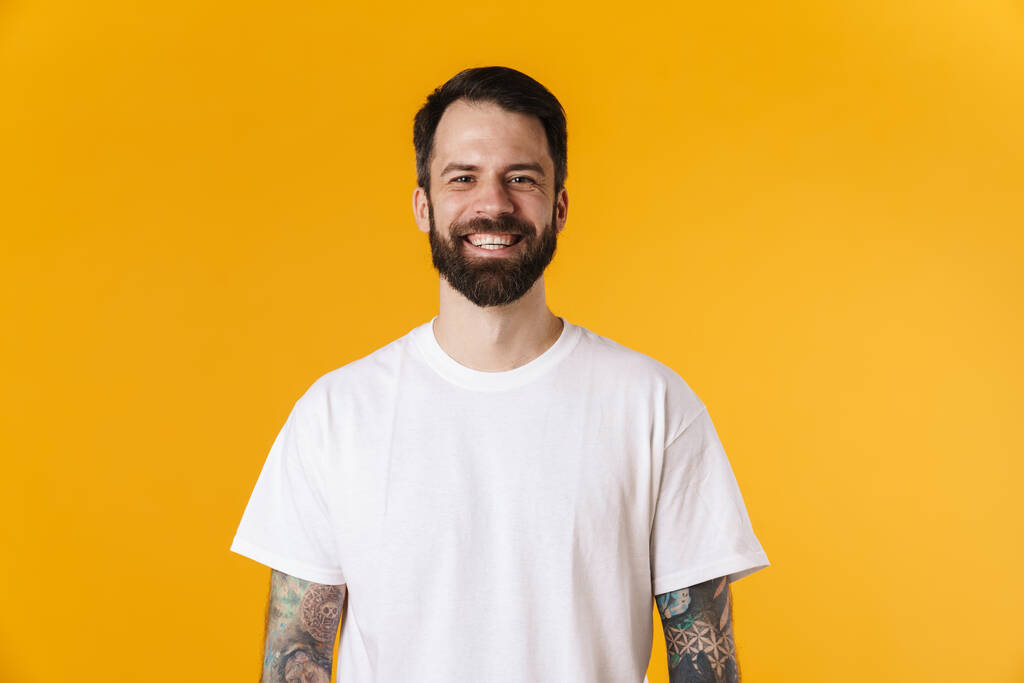 Портрет счастливой брюнетки бородатого мужчину, стоящего над желтой стеной, смотрящего в камеру - Фото, изображение