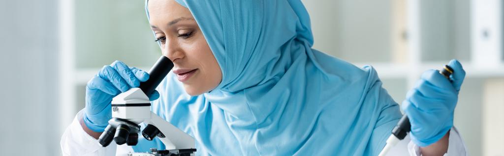 Muslimischer Wissenschaftler in medizinischer Maske mit Pipette und Blick durchs Mikroskop, Banner  - Foto, Bild