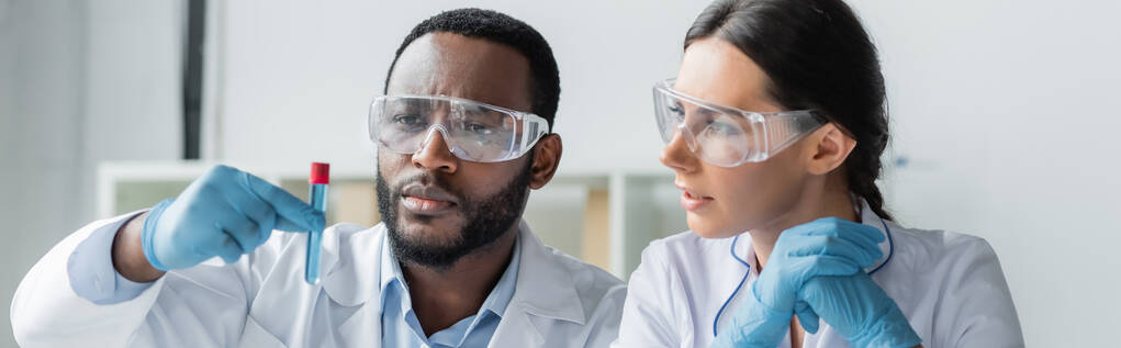 Cientistas multiétnicos em luvas de látex e óculos olhando para tubo de ensaio em laboratório, banner  - Foto, Imagem