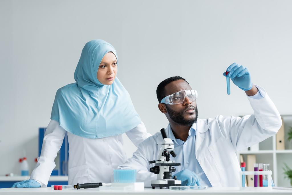 Interracial scientists in latex gloves looking at sample near microscope in laboratory  - Fotó, kép