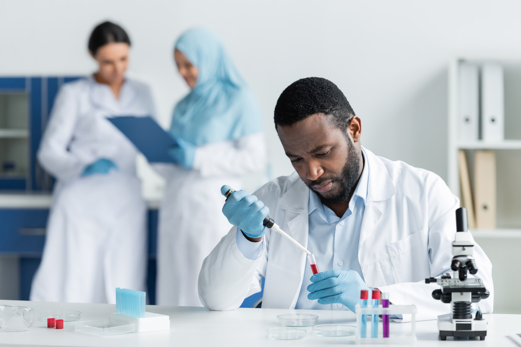African american scientist researching samples in test tubes near blurred colleagues in lab - Fotó, kép