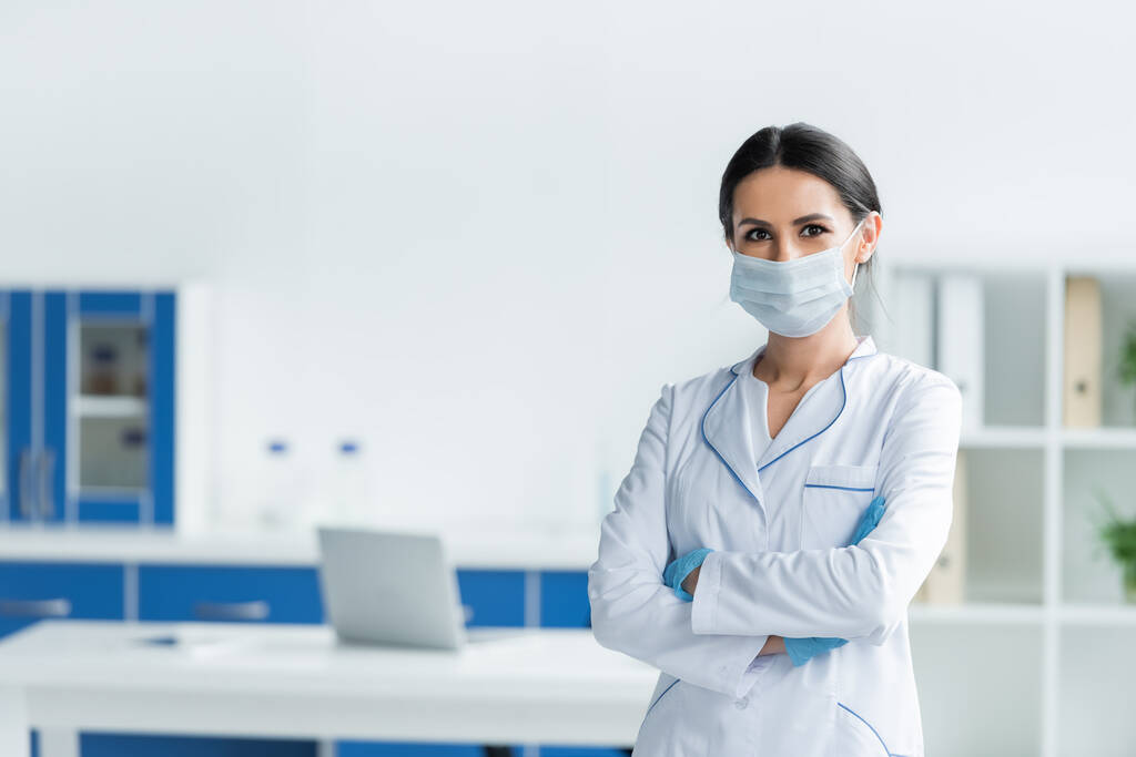 Лікар в латексних рукавичках і медичній масці, що стоїть з схрещеними руками в лікарні
  - Фото, зображення