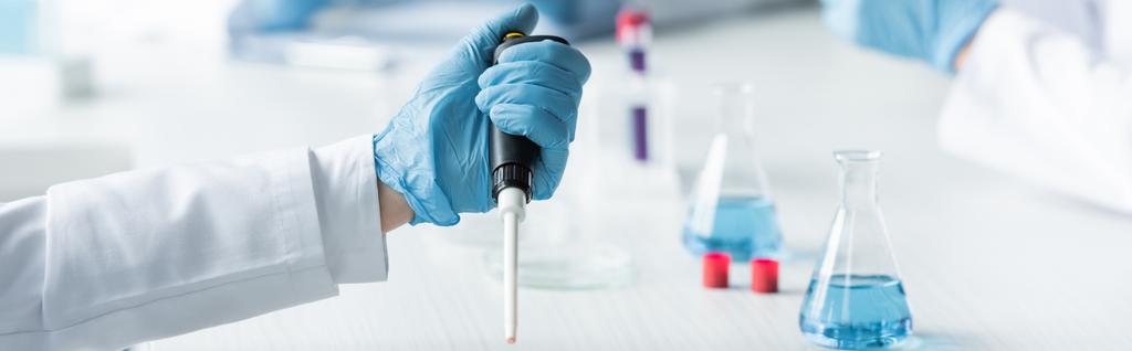 Cropped view of scientist in latex glove holding electronic pipette near flasks, banner  - Fotografie, Obrázek