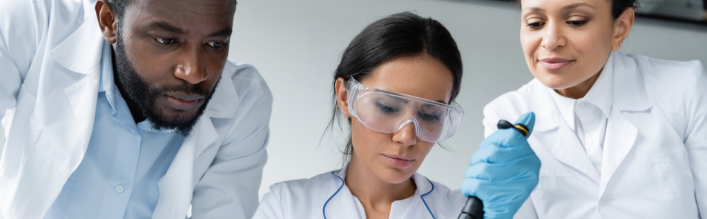 учёный в очках держит пипетку рядом с межрасовыми коллегами, баннер  - Фото, изображение