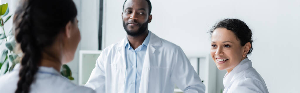 Afrikaanse amerikaanse arts glimlachen naar collega in kliniek, banner  - Foto, afbeelding