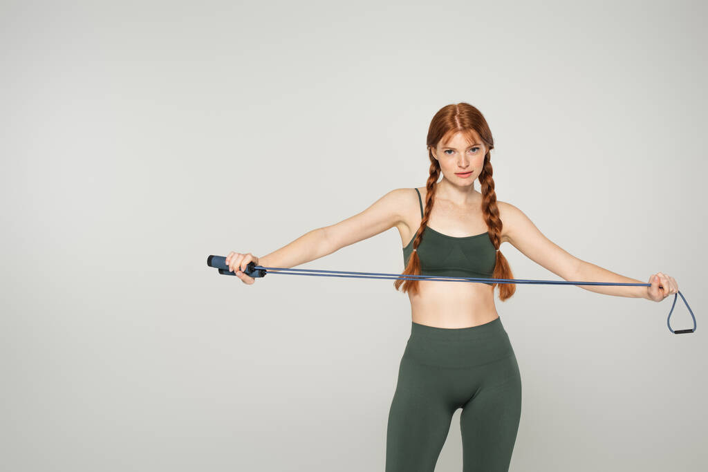 Sportswoman with freckles holding skipping rope isolated on grey  - Photo, Image