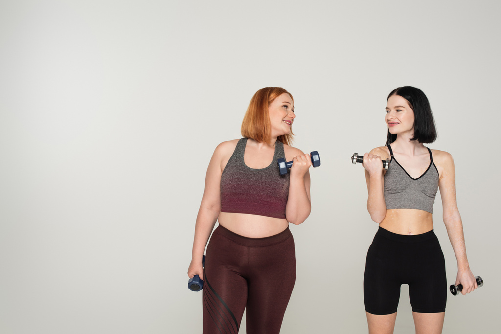 Vrolijk lichaam positieve sportenvrouwen training met halters geïsoleerd op grijs  - Foto, afbeelding