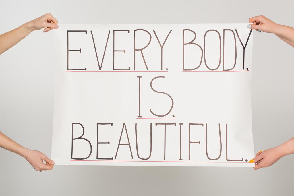 Cropped view of women holding placard with every body is beautiful lettering isolated on grey  - Photo, Image