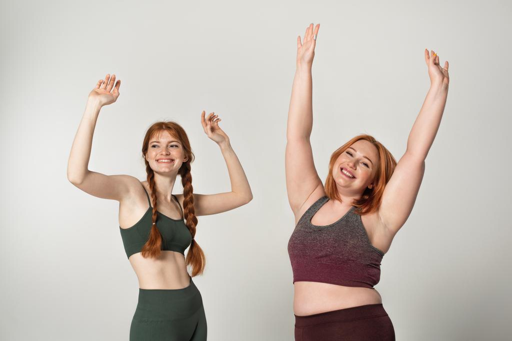 Corpo sorridente esportistas positivos levantando as mãos isoladas no cinza  - Foto, Imagem