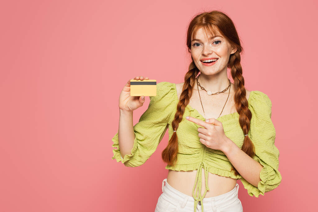 笑顔redhead女性pointingでクレジットカード絶縁上のピンク  - 写真・画像