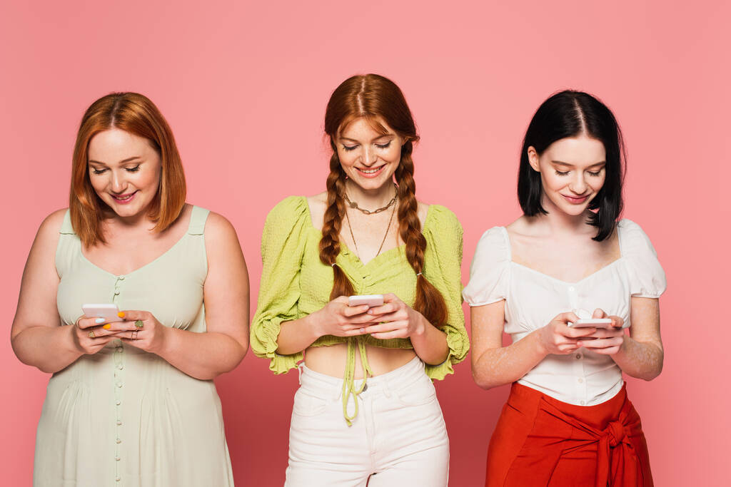 Χαμογελώντας σώμα θετικές γυναίκες χρησιμοποιώντας smartphones απομονώνονται σε ροζ  - Φωτογραφία, εικόνα