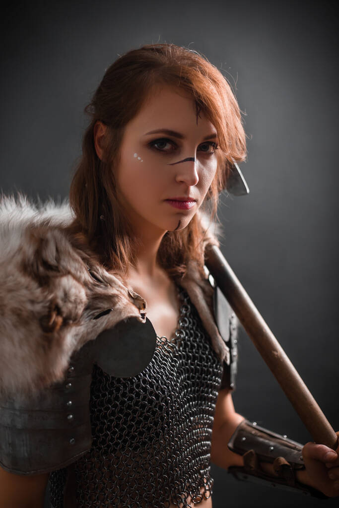斧で武装した鎧を着た中世のファンタジー女性戦士の肖像画、黒の背景に暗いスタジオでポーズ. - 写真・画像