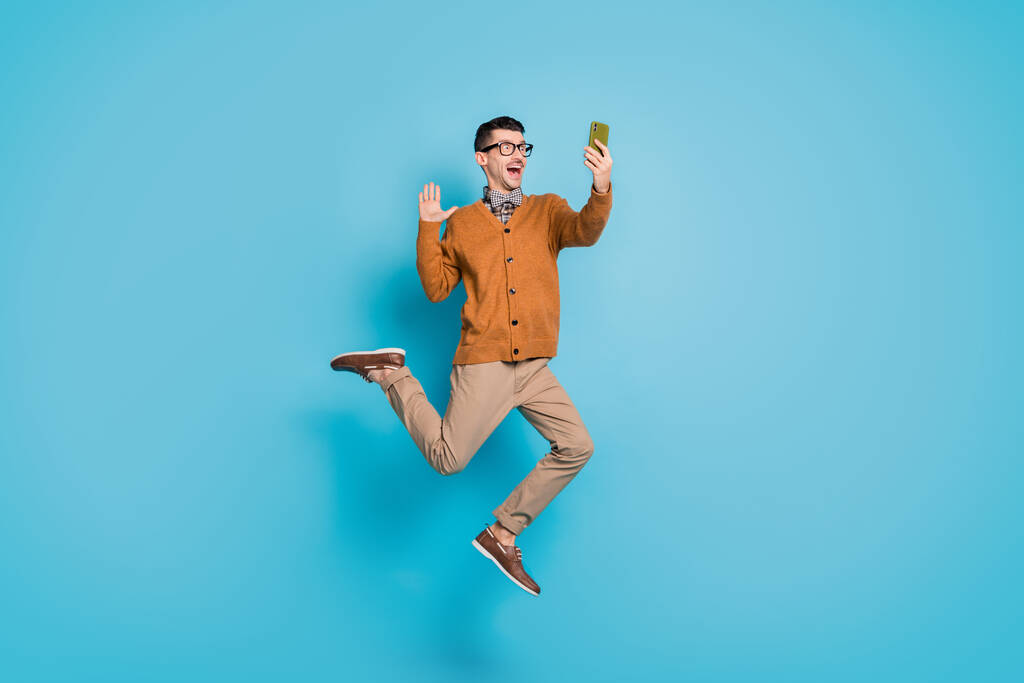 In voller Länge Foto von jungen aufgeregten Mann springen Welle hallo machen Selfie videocall Handy isoliert über blauen Farbhintergrund - Foto, Bild