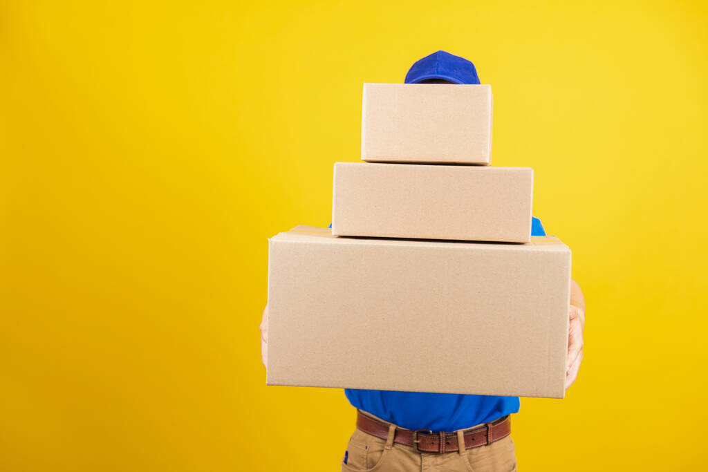 Portrait excited attractive delivery happy man logistic standing he smile wearing blue t-shirt and cap uniform holding parcel box looking to camera, studio shot isolated on yellow background - Photo, Image